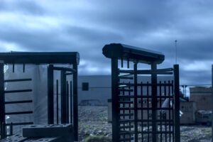 Exterior of an industrial site, turnstiles in foreground and a big industrial building in the back. The sky is exceptionally blue.