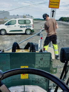 A worker is putting a traffic signs into place on a huge gravel parking lot next to an industrial building.